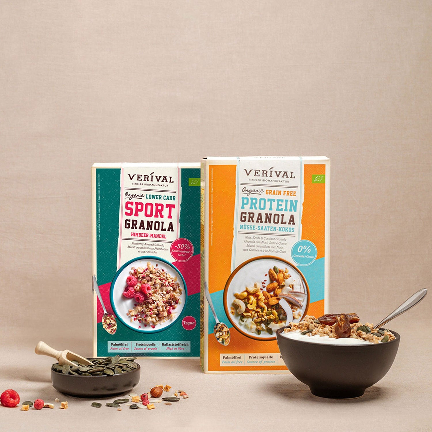 Deux boîtes de granola Verival (Sport Granola et Protein Granola) se trouvent derrière un bol de granola avec une cuillère et un petit bol de graines sur un fond neutre.
