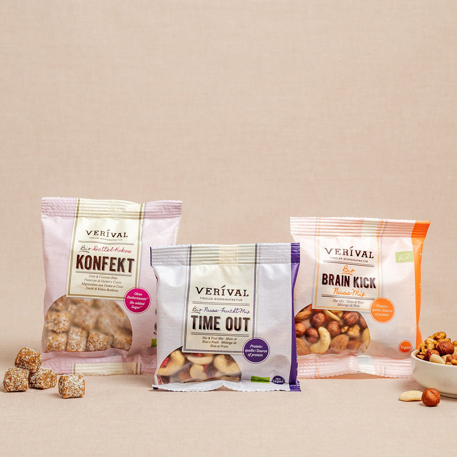 Trois packs de collations Verival – Konfekt, Time Out et Brain Kick – sont présentés debout sur une surface neutre, avec une partie de leur contenu dispersé à proximité.