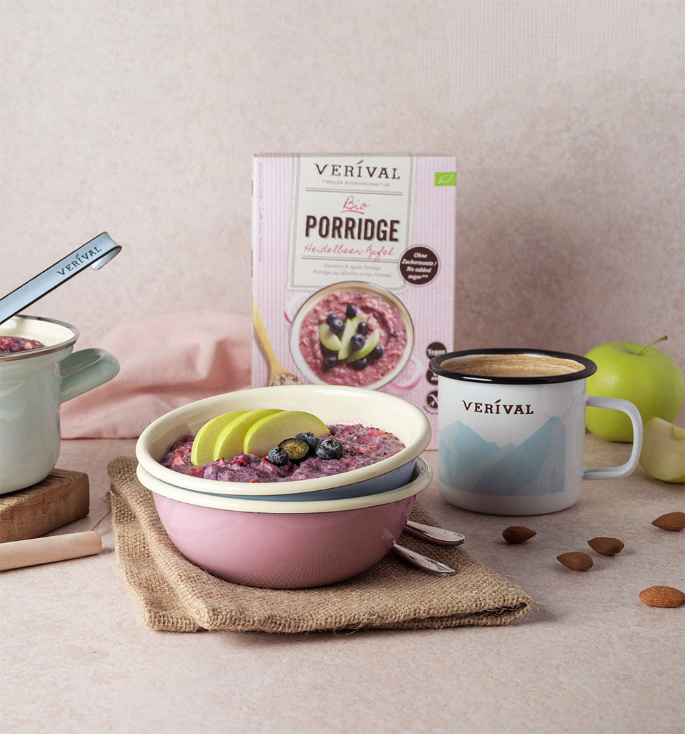 Trois boîtes de porridge bio Verival aux saveurs différentes se trouvent à côté d'un pot de porridge prêt à l'emploi, de fraises, de tranches de pomme et d'un bol de graines de chia.
