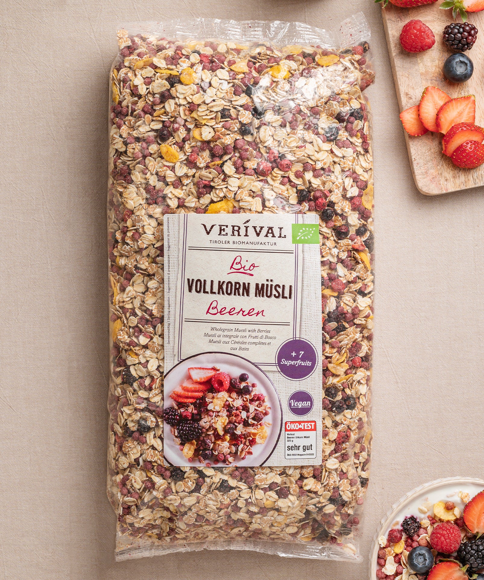 Eine Packung Beeren Vollkorn Müsli von Verival Bio steht auf einem Tisch und punktet mit seinen biologischen, ballaststoffreichen Zutaten und Superfrüchten. Daneben stehen Müslischalen mit buntem Obst.