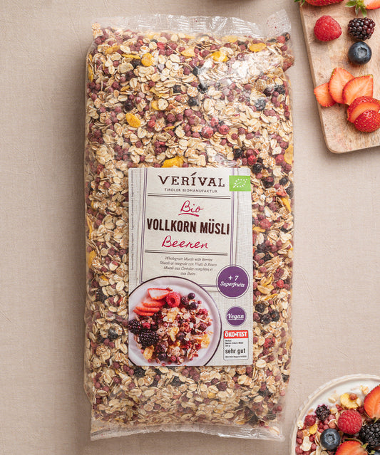 Eine Packung Beeren Vollkorn Müsli von Verival Bio steht auf einem Tisch und punktet mit seinen biologischen, ballaststoffreichen Zutaten und Superfrüchten. Daneben stehen Müslischalen mit buntem Obst.