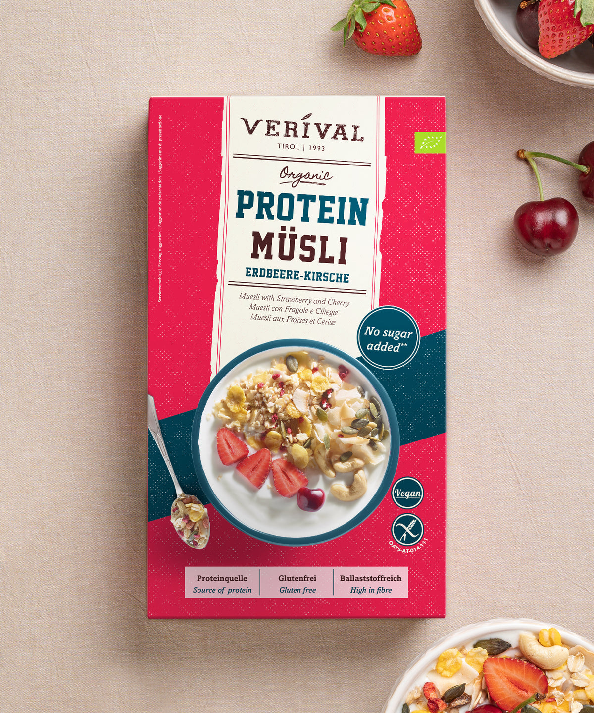 Eine Packung Bio Erdbeere-Kirsche Protein-Müsli der Verival Bio GmbH, auf deren Verpackung eine Schüssel mit Joghurt, Obst und Nüssen zu sehen ist, umgeben von frischen Erdbeeren und Kirschen; das Produkt wird als pflanzliche Proteinquelle ohne Zuckerzusatz ausgewiesen.