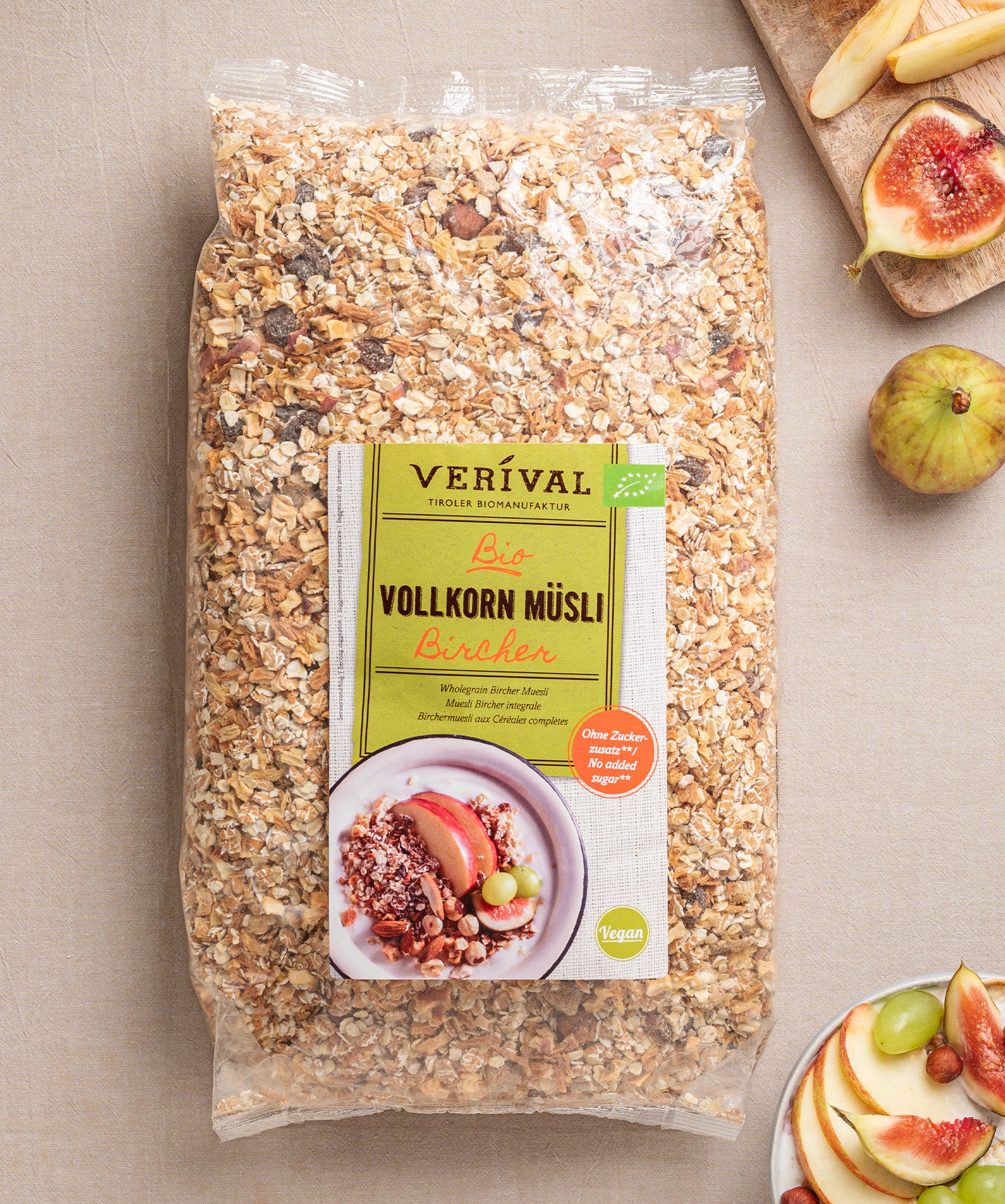 Eine Packung ballaststoffreiches Bircher Vollkorn Müsli von Verival Bio  steht einladend neben einem Teller mit Apfelscheiben und Feigen auf dem Tisch.