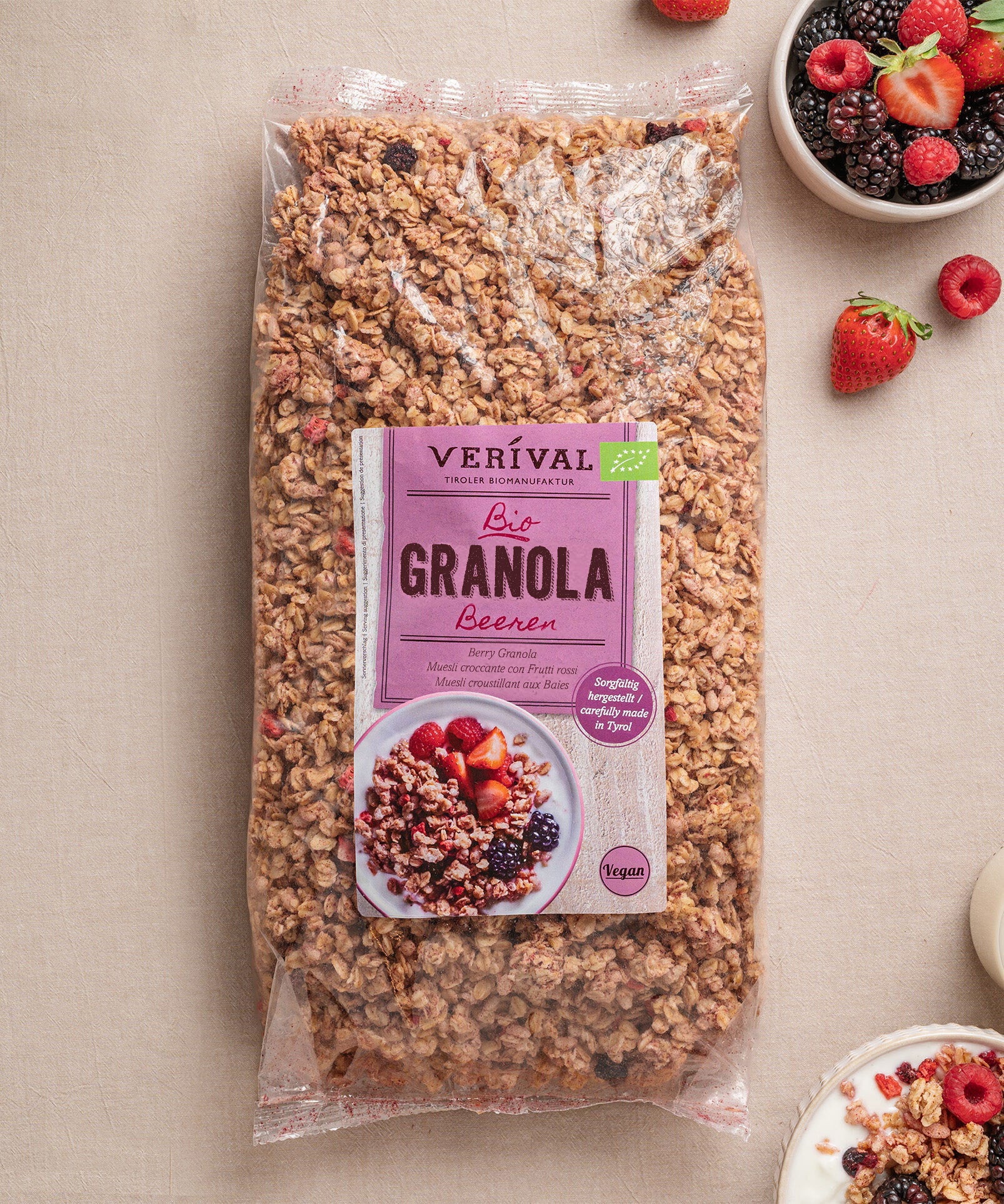 Eine Packung Beeren-Granola von Verival Bio steht auf dem Tisch, umgeben von frischen Beeren und Joghurt. Perfekt für ein veganes Frühstücksfestmahl.