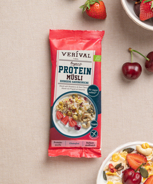 Die Einzeloportionspackung Protein Müsli Erdbeere-Sauerkirsche von Verival Bio hat eine leuchtend roten Verpackung mit einer Abbildung frischenr Erdbeeren, Kirschen und einer Schüssel Müsli daneben – eine ideale pflanzliche Proteinquelle für einen gesunden Tag.