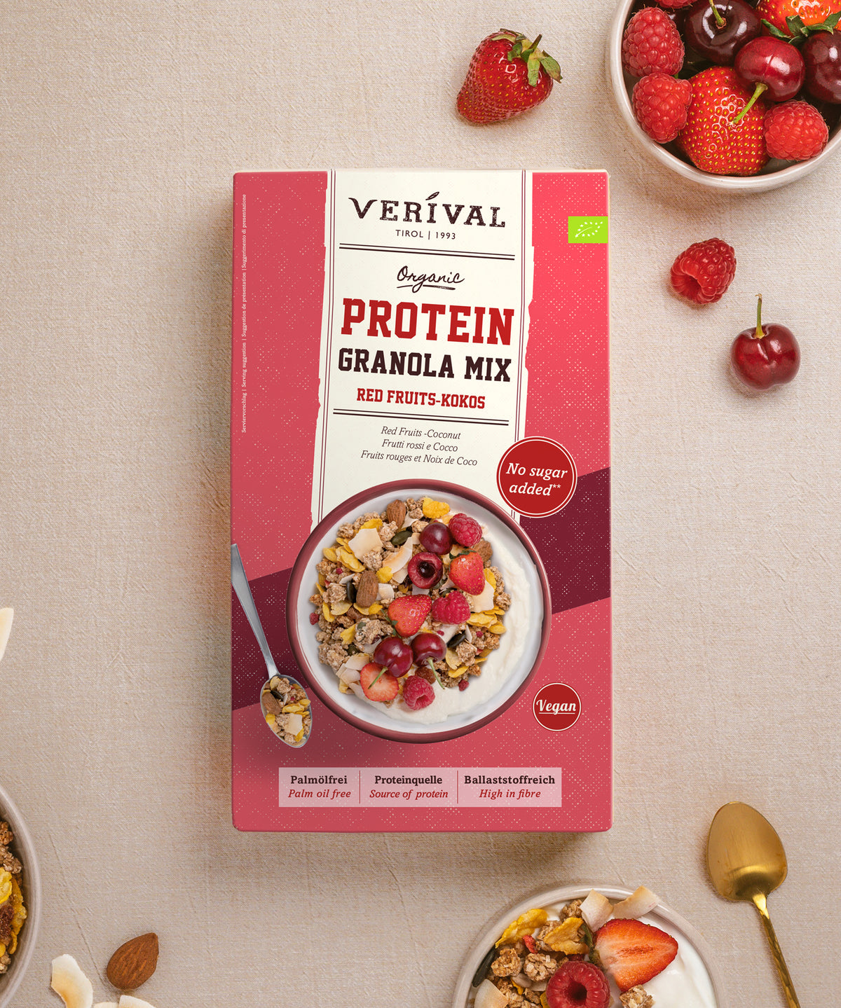 Verpackung mit Verival Bio Bio Red Fruits Protein Granola Mix – eine Schüssel ballaststoffreiches Müsli mit roten Beeren und Kokosnuss, umgeben von frischen Erdbeeren, Himbeeren und Kirschen.