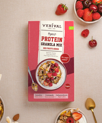 Verpackung mit Verival Bio Bio Red Fruits Protein Granola Mix – eine Schüssel ballaststoffreiches Müsli mit roten Beeren und Kokosnuss, umgeben von frischen Erdbeeren, Himbeeren und Kirschen.